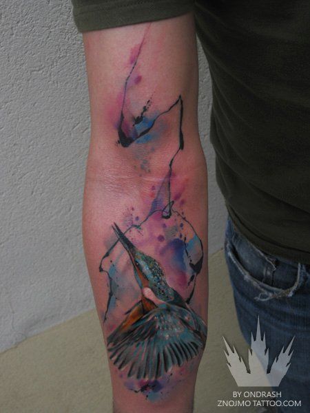 A blue kingfisher flies among splatters of paint in this abstract watercolor tattoo by Ondrash