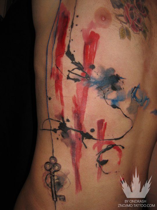 A key hangs suspended from splatters of ink in this abstract watercolor tattoo by Ondrash