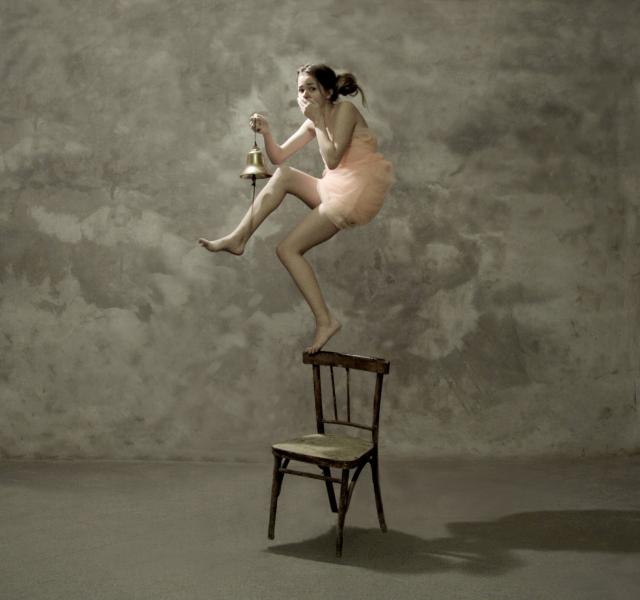 A Katerina Bodrunova photograph of a girl standing on the back of a chair ringing a bell