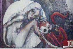 A graffiti painting by German artist Herakut of a nude girl in the moon with a pet monkey and a saying about beauty and love