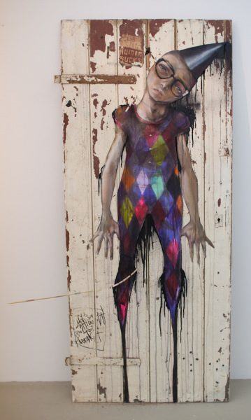 An emotive painting on an old door by Herakut of a jester wearing glasses hanging by his neck