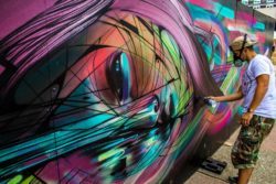Street artist Hopare at work on one of his colorful graphic design influenced graffiti murals of a pretty girl
