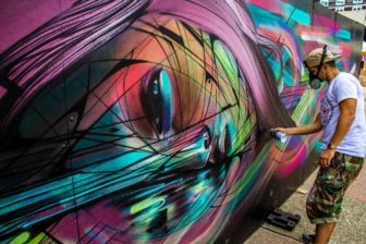 Street artist Hopare at work on one of his colorful graphic design influenced graffiti murals of a pretty girl
