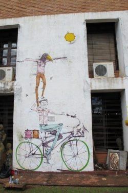Mart Aire balances a bird headed man on a cyclist in this circus themed street art mural