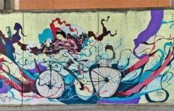 One of Mart Aire's street art cyclists rides through a swarm of creative swirls of color in this captivating graffiti mural