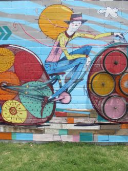 Street artist Mart Aire creates a cheerful graffiti mural feeaturing a happy guy on a bicycle.